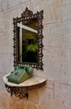 A vintage green rotary phone on a marble shelf with a decorative mirror.