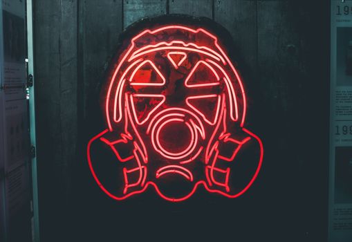Illuminated neon gas mask sign in a dark urban setting. Perfect for themes of urban art and industrial decor.