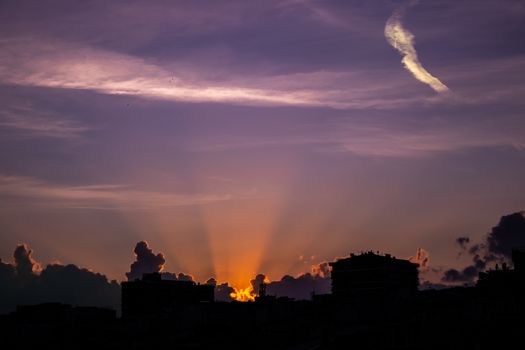 Silhouetted city buildings under a dramatic sunset sky with vibrant colors.