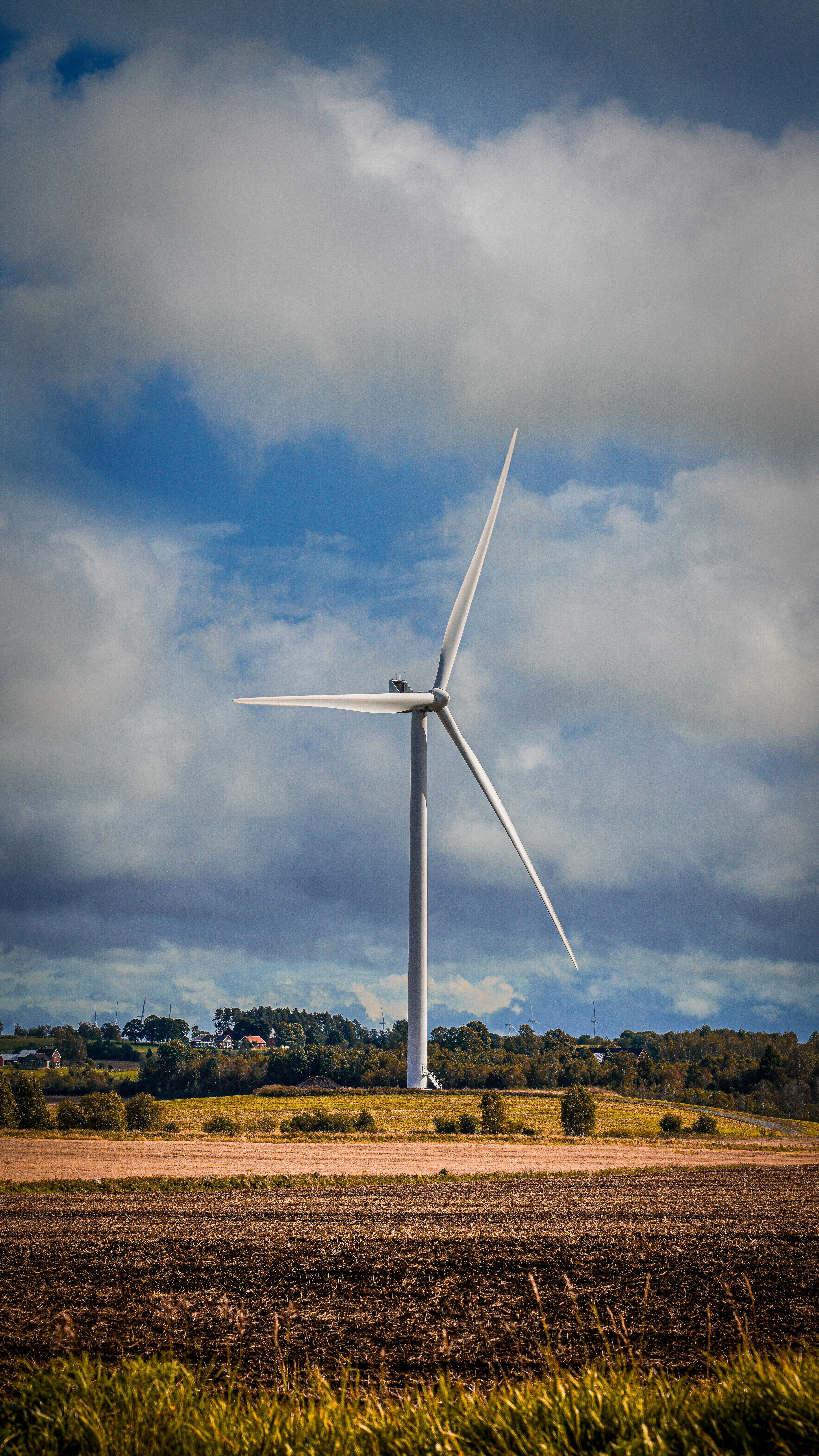 A tall wind turbine stands in an open field under a partly cloudy sky, symbolizing clean energy.