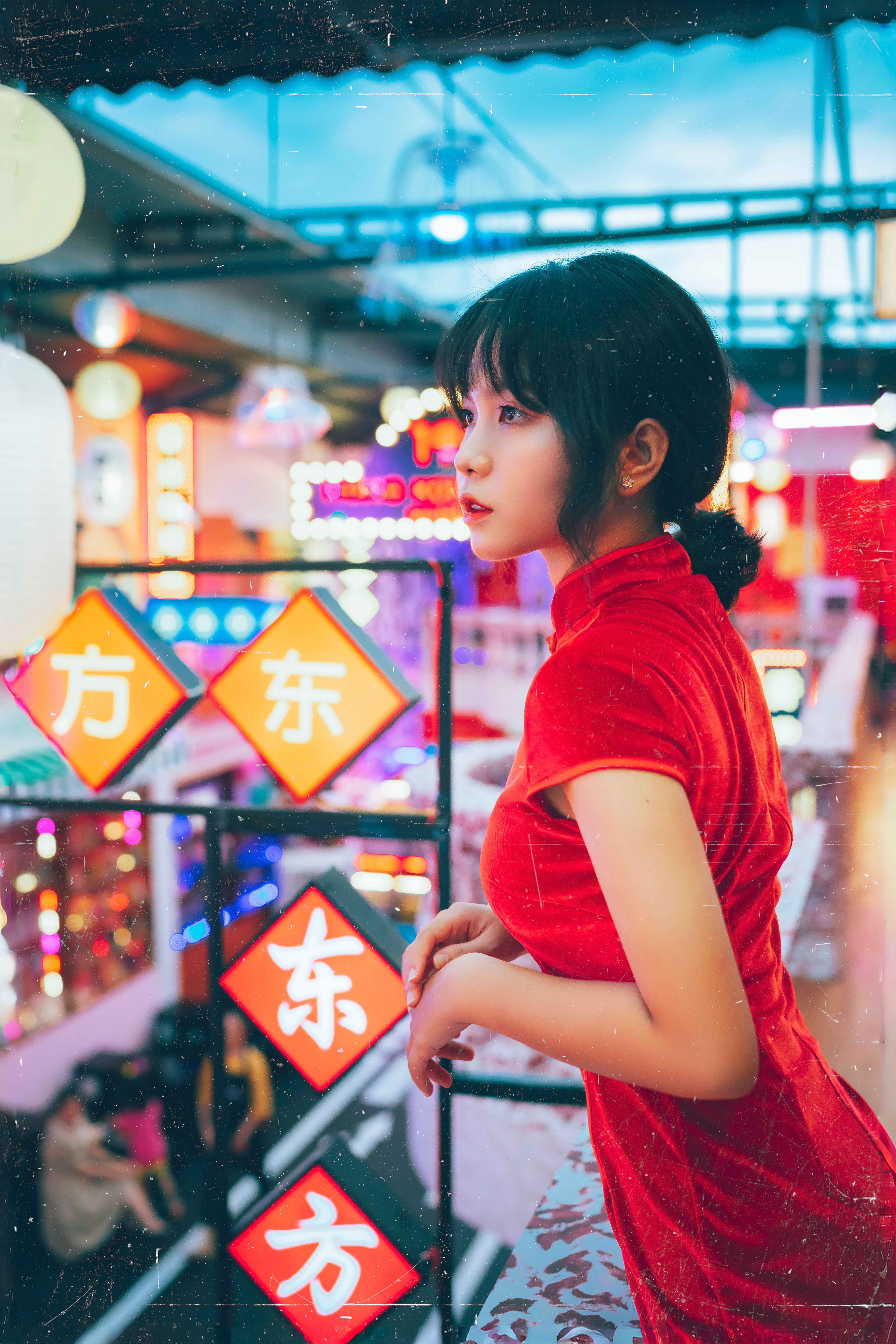 Young woman in red dress gazes in a vibrant neon-lit market area, exuding an urban and colorful ambiance.