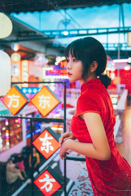 Young woman in red dress gazes in a vibrant neon-lit market area, exuding an urban and colorful ambiance.