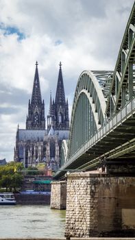 A stunning view of Cologne Cathedral next to the Hohenzollern Bridge on a bright day.