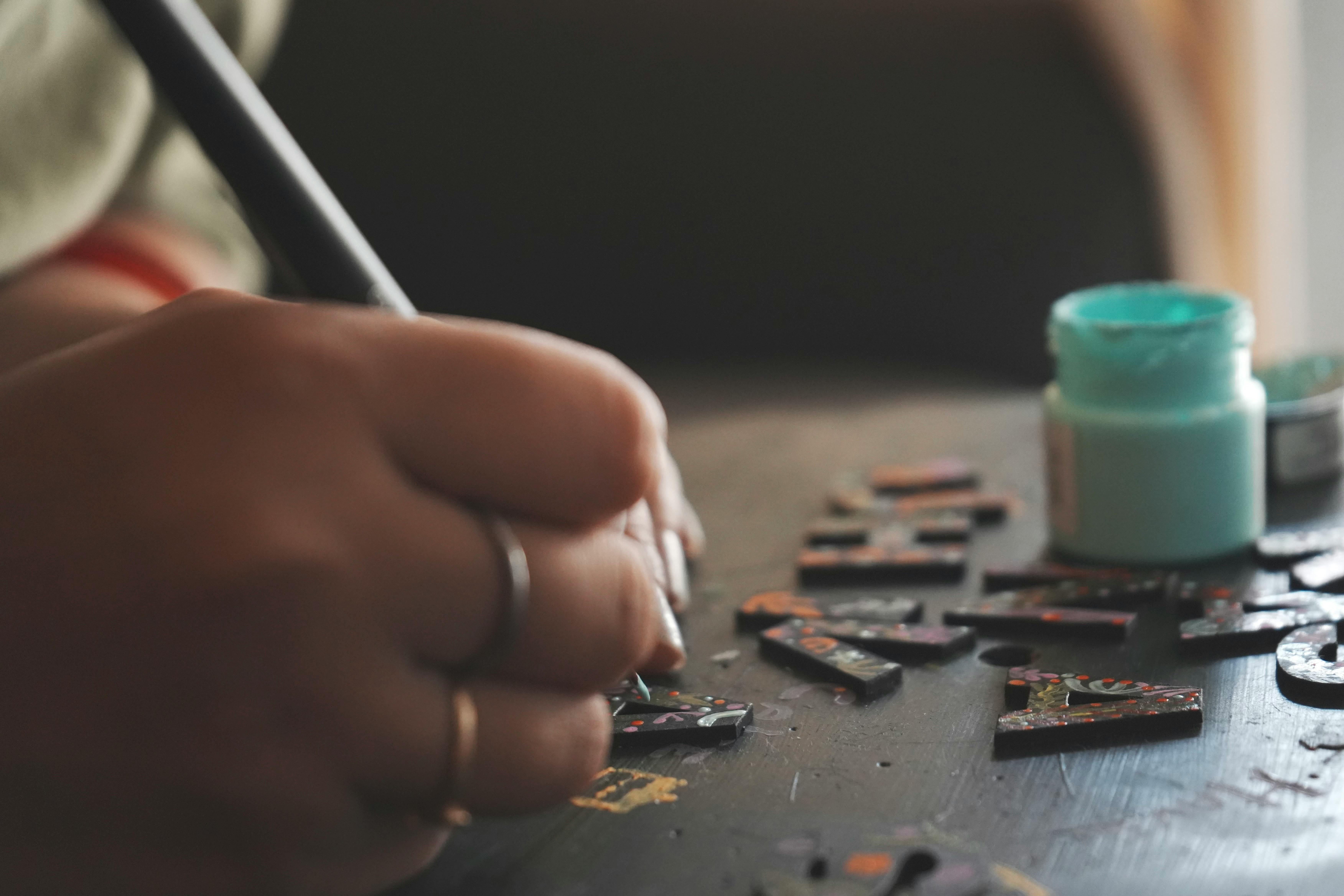 Person painting intricate designs on wooden letters with acrylic paint. Artistic process close-up.