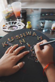 Hands decorating letters with flowers on a black canvas using craft supplies.