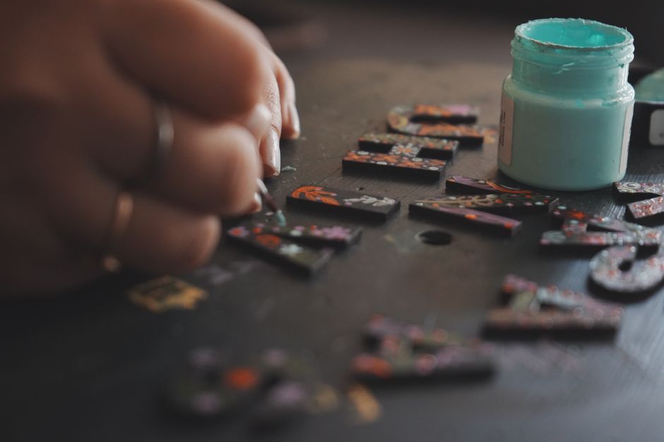 Entryway Key and Mail Station DIY home decor project — A hand paints wooden letters with artistic designs using blue paint on a dark surface.