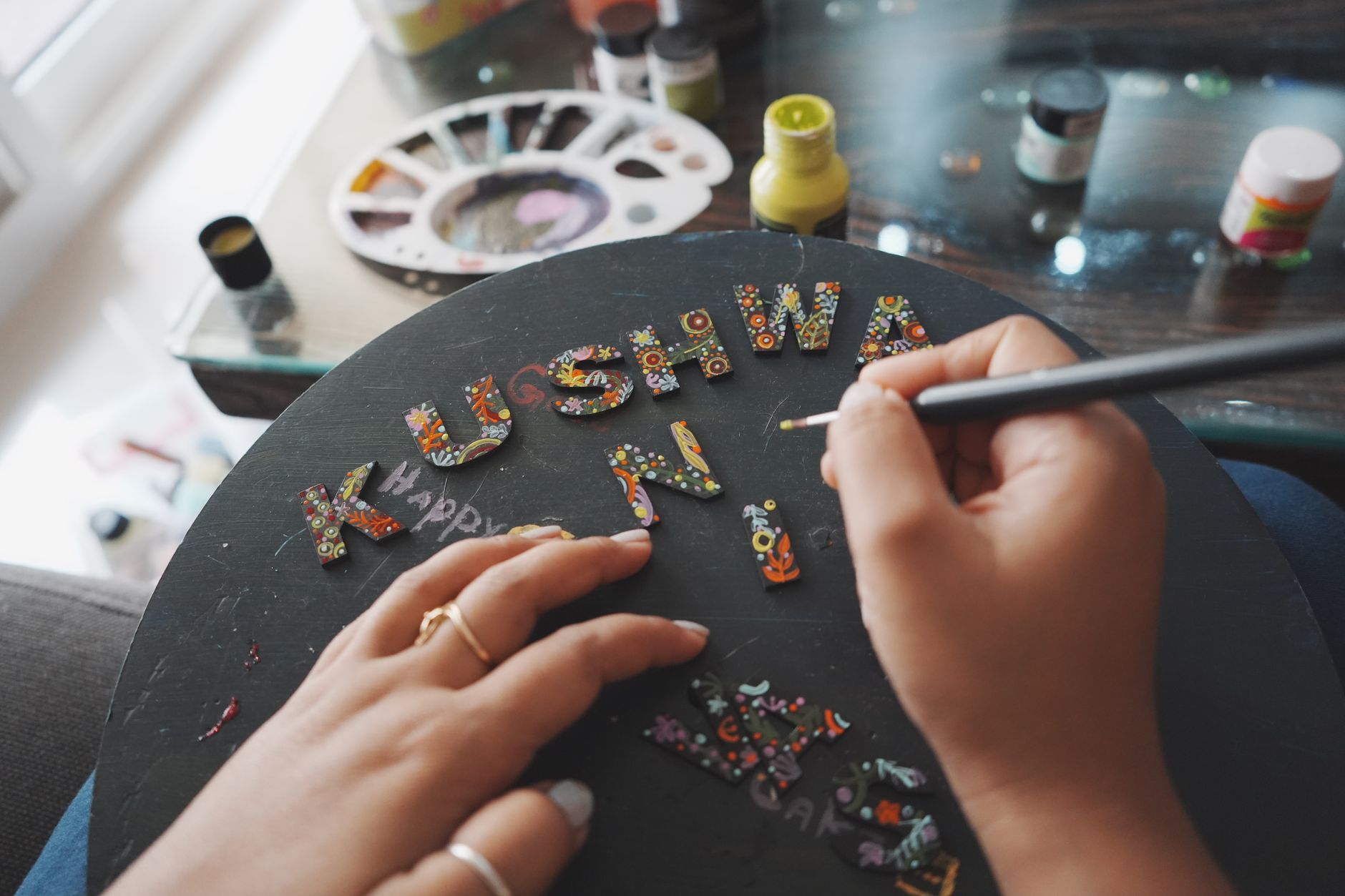 Close-up of a hand painting decorative letters with intricate designs on a board.