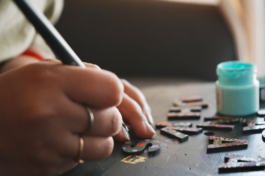 Hands painting wooden letters with precision, showcasing a creative DIY project.
