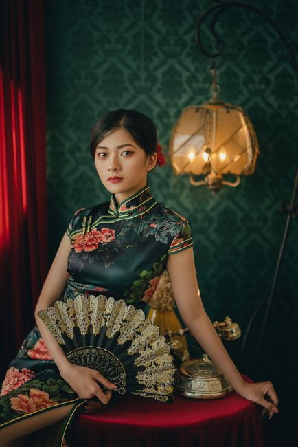 Portrait of a woman in a floral cheongsam holding a decorative fan in a vintage setting.