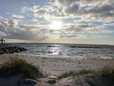 Peaceful beach scene with grasses, waves, and the sun setting over the ocean.