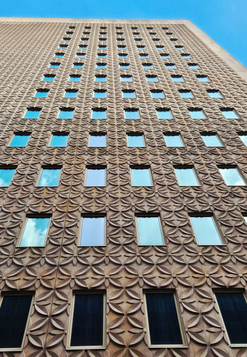 Free A low-angle view of a modern building featuring a geometric patterned facade under a clear blue sky. Stock Photo