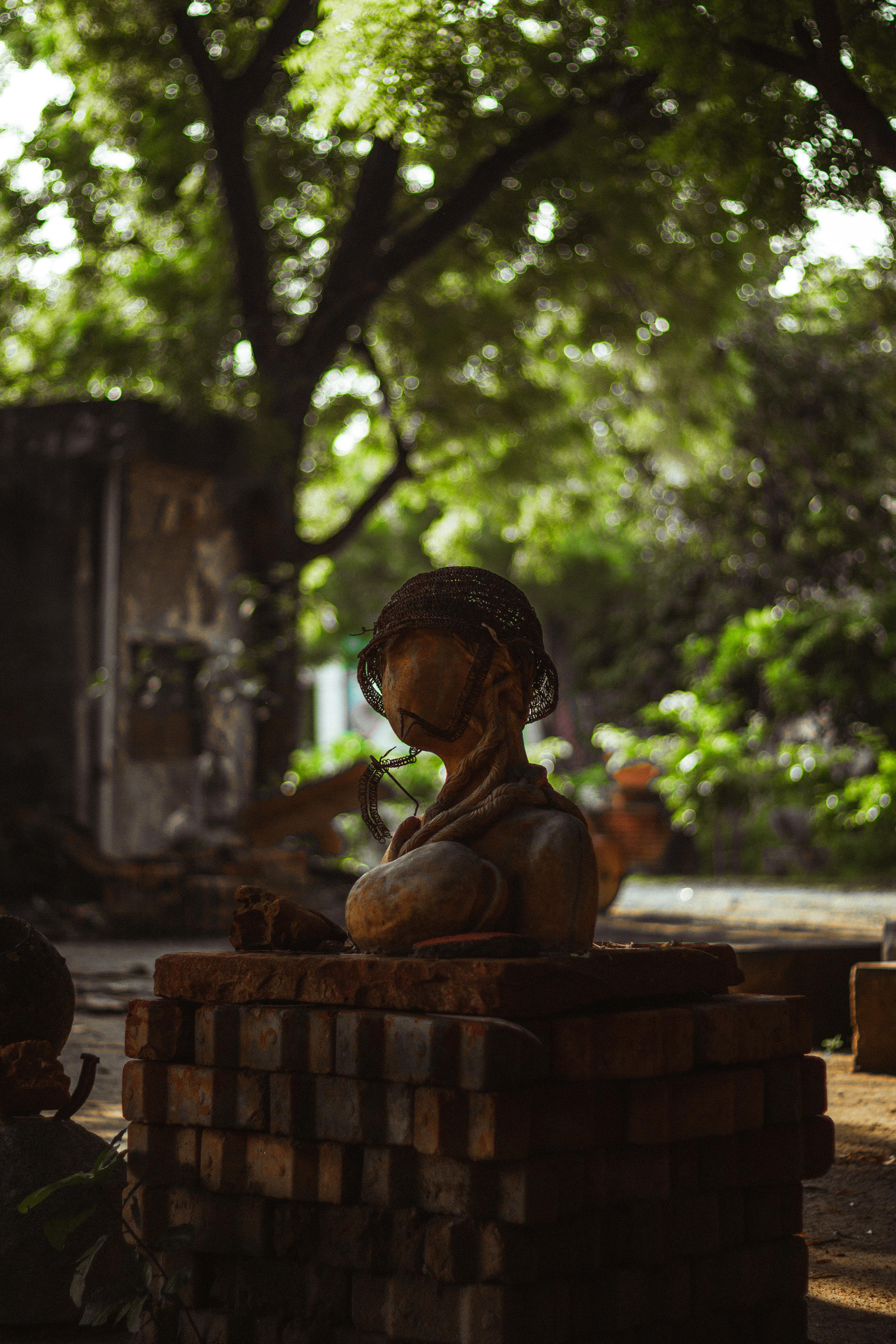 Moss covered statue in a serene outdoor garden with a brick base.