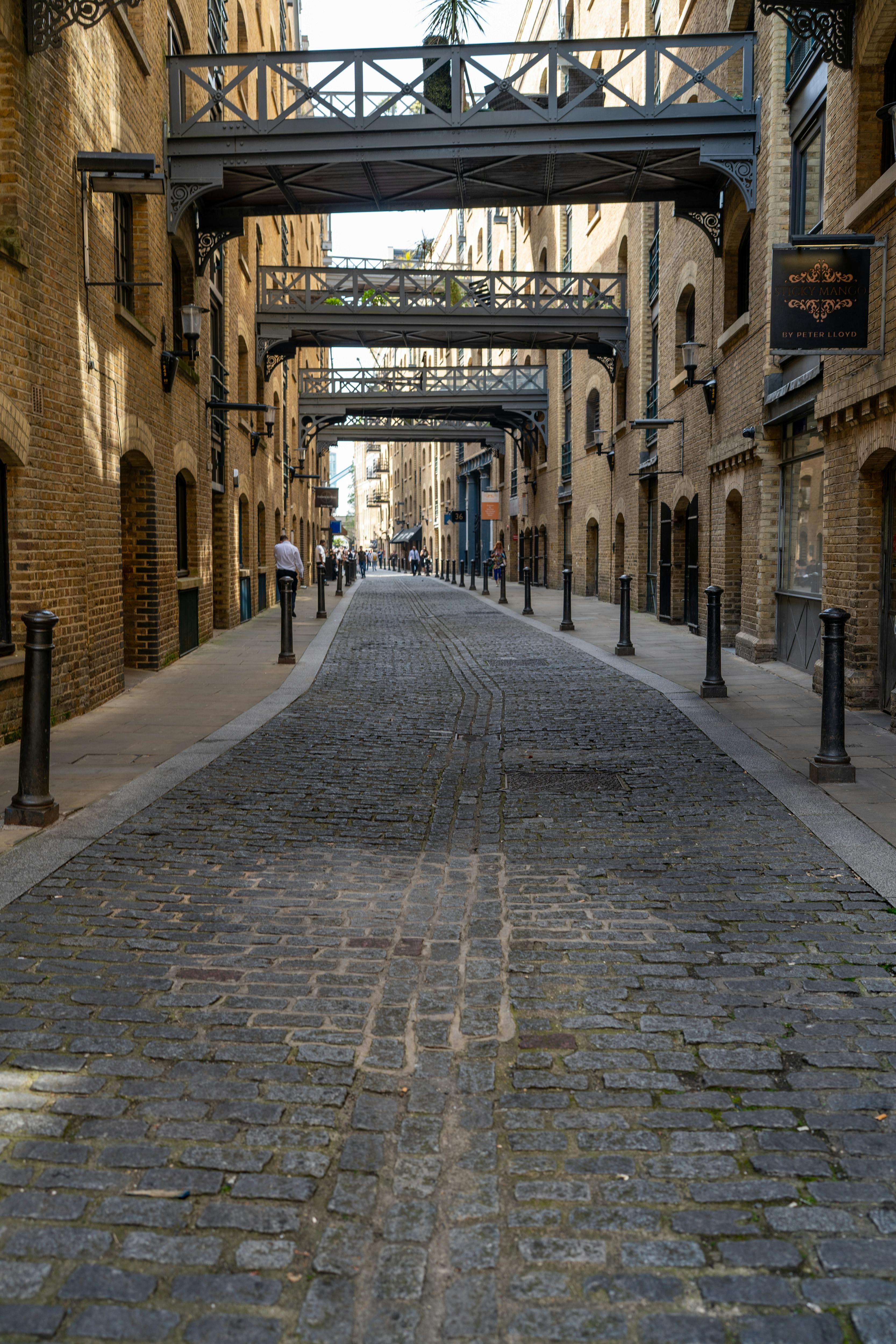 Cobblestone street with overhead bridges in Shad Thames, London, showcasing historic architecture.
