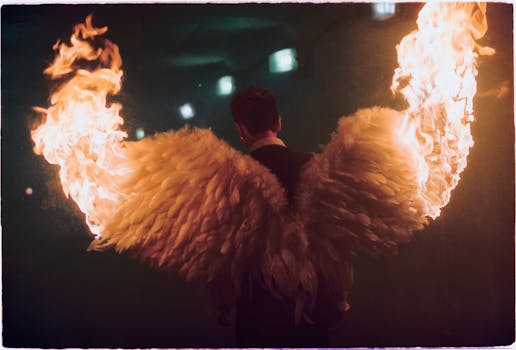 Back view of a man wearing feathered angel wings on fire in a dark setting.