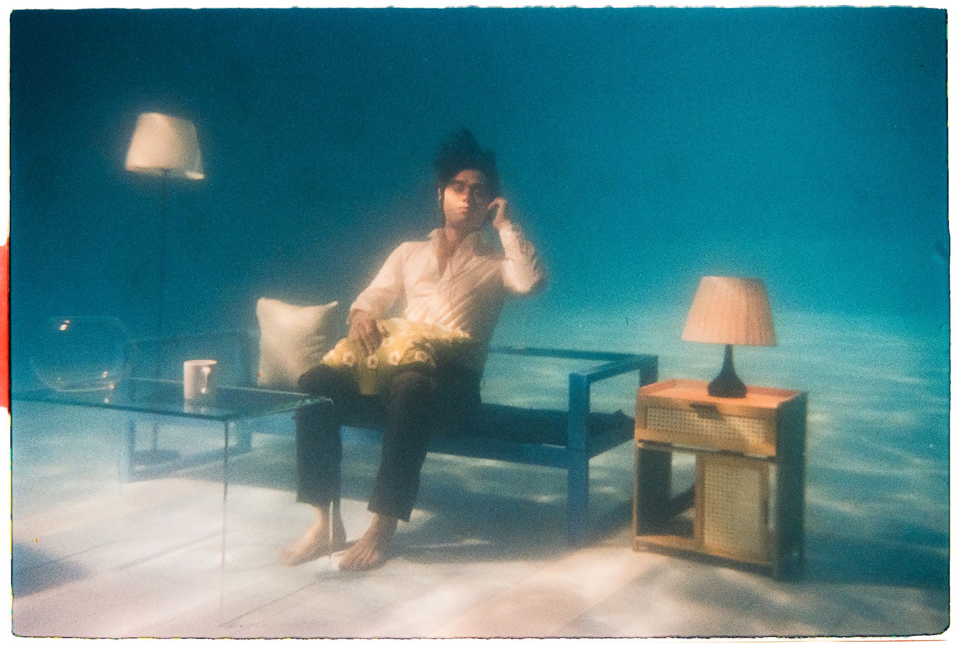 A man sits in a living room setup underwater, creating a surreal and artistic scene.