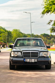 A classic black sedan parked outdoors under sunny skies with a scenic backdrop.