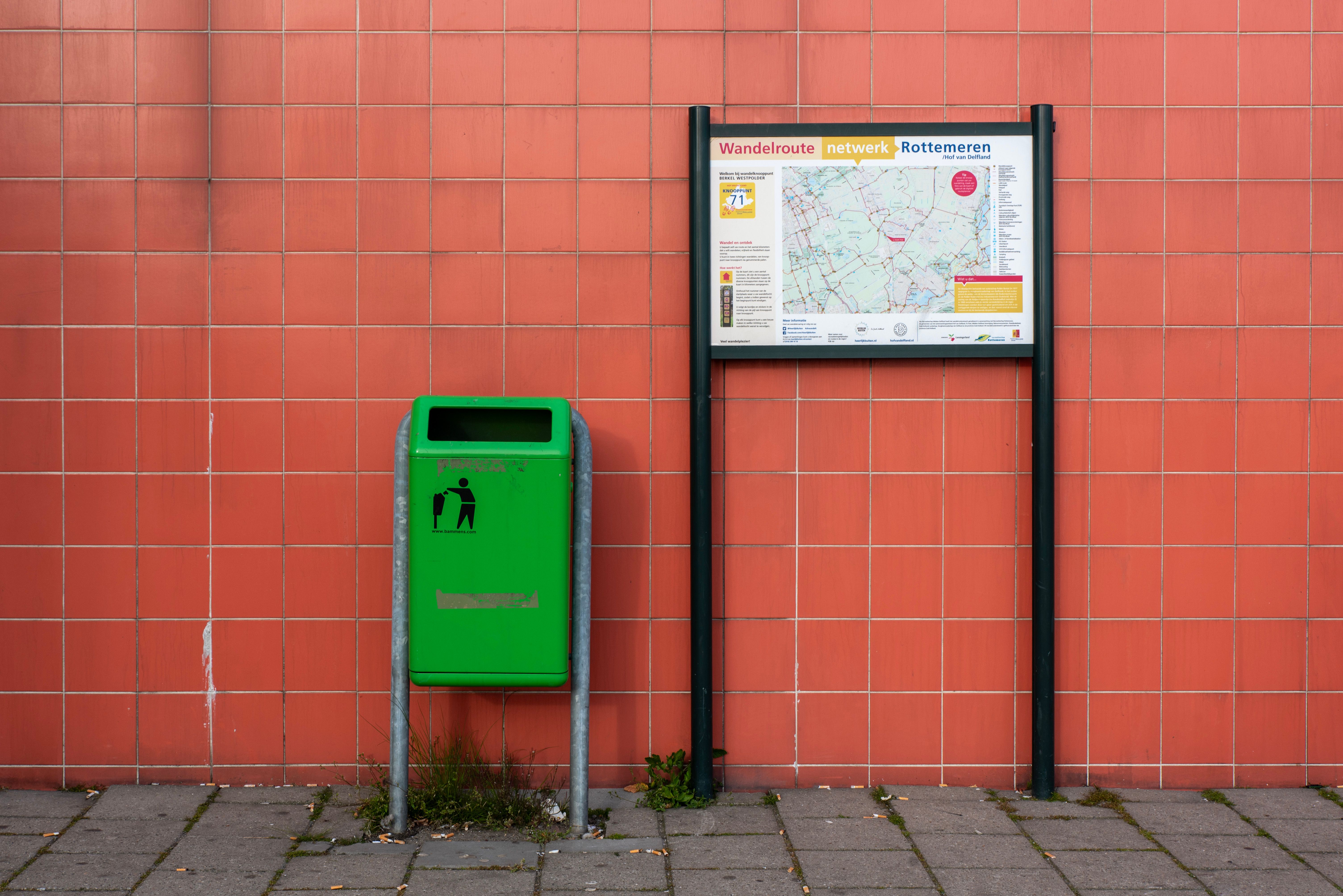 Green trash bin and map sign on red tiled wall highlighting public cleanliness.