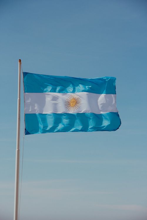 Free A vibrant Argentinian flag flutters in the clear blue sky, symbolizing national pride. Stock Photo