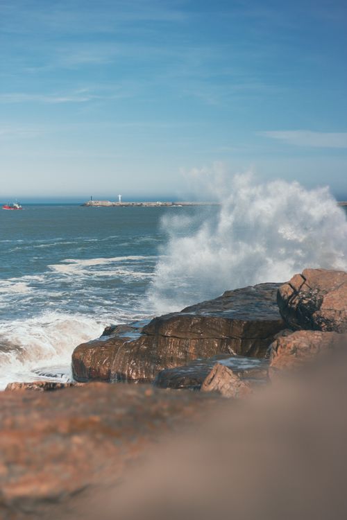 Free Dramatic ocean waves hit the rocky shore under a clear blue sky, perfect for coastal themes. Stock Photo