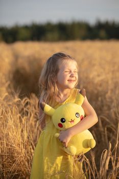 Young girl smiling in a wheat field with a Pikachu plush toy under sunlight.