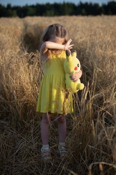 Young girl in a sunny wheat field embraces a plush toy, capturing a moment of innocence.