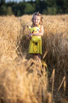 A young girl holds a Pikachu toy in a sunlit wheat field, capturing a serene summer moment.