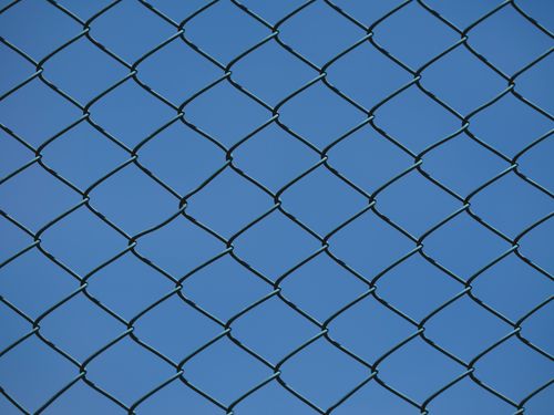бесплатная Крупный план металлического сетчатого ограждения на фоне ясного голубого неба, символизирующего городскую безопасность и границы. Стоковое фото