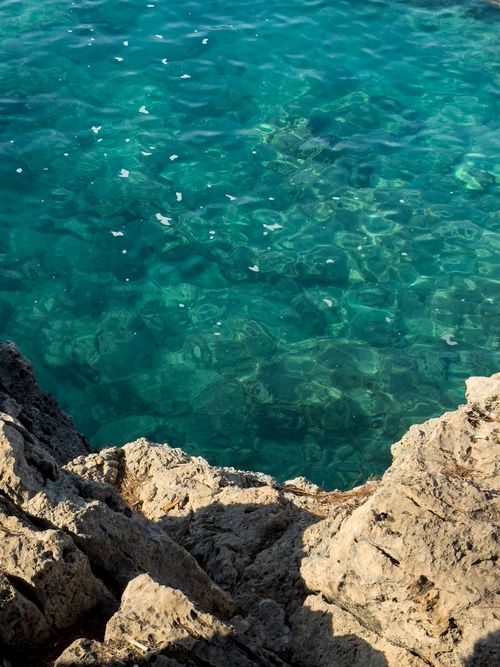 Free Stunning view of clear turquoise waters and rugged rocky shoreline on a sunny day. Stock Photo