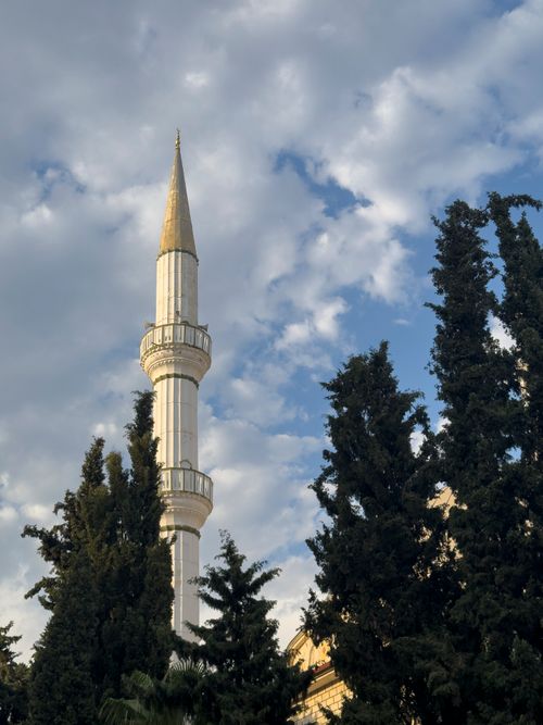 Free A striking minaret rising against a blue sky, framed by lush trees, capturing a serene moment. Stock Photo