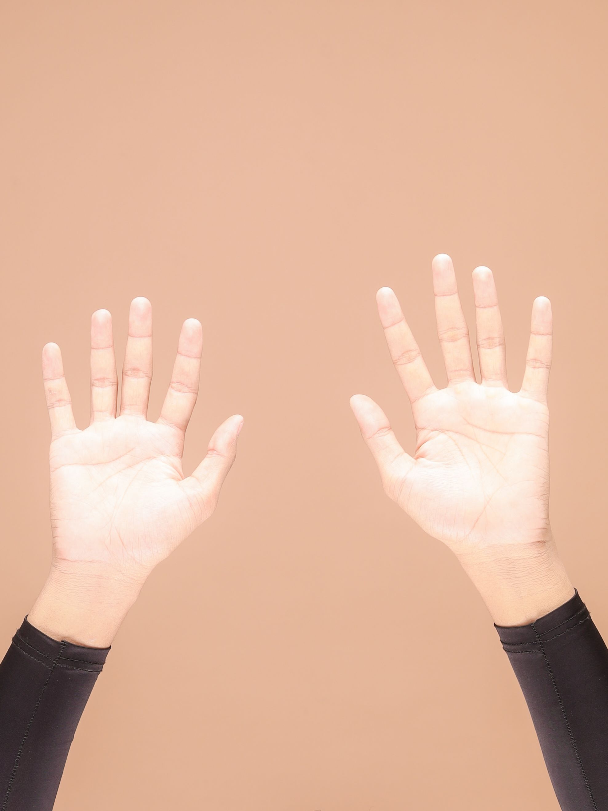 Two hands raised with palms open against a soft brown background, symbolizing openness.
