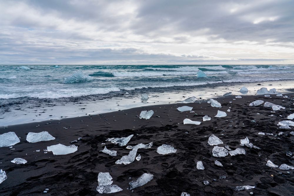 Blocuri de gheață strălucind pe nisipul negru la Diamond Beach, Islanda