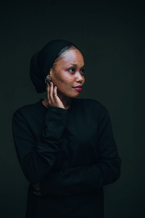 Free A thoughtful African woman in a dark hijab stands against a neutral background, exuding modern style. Stock Photo