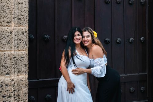 Free Two women standing and smiling near a historic stone and wooden doorway. Stock Photo