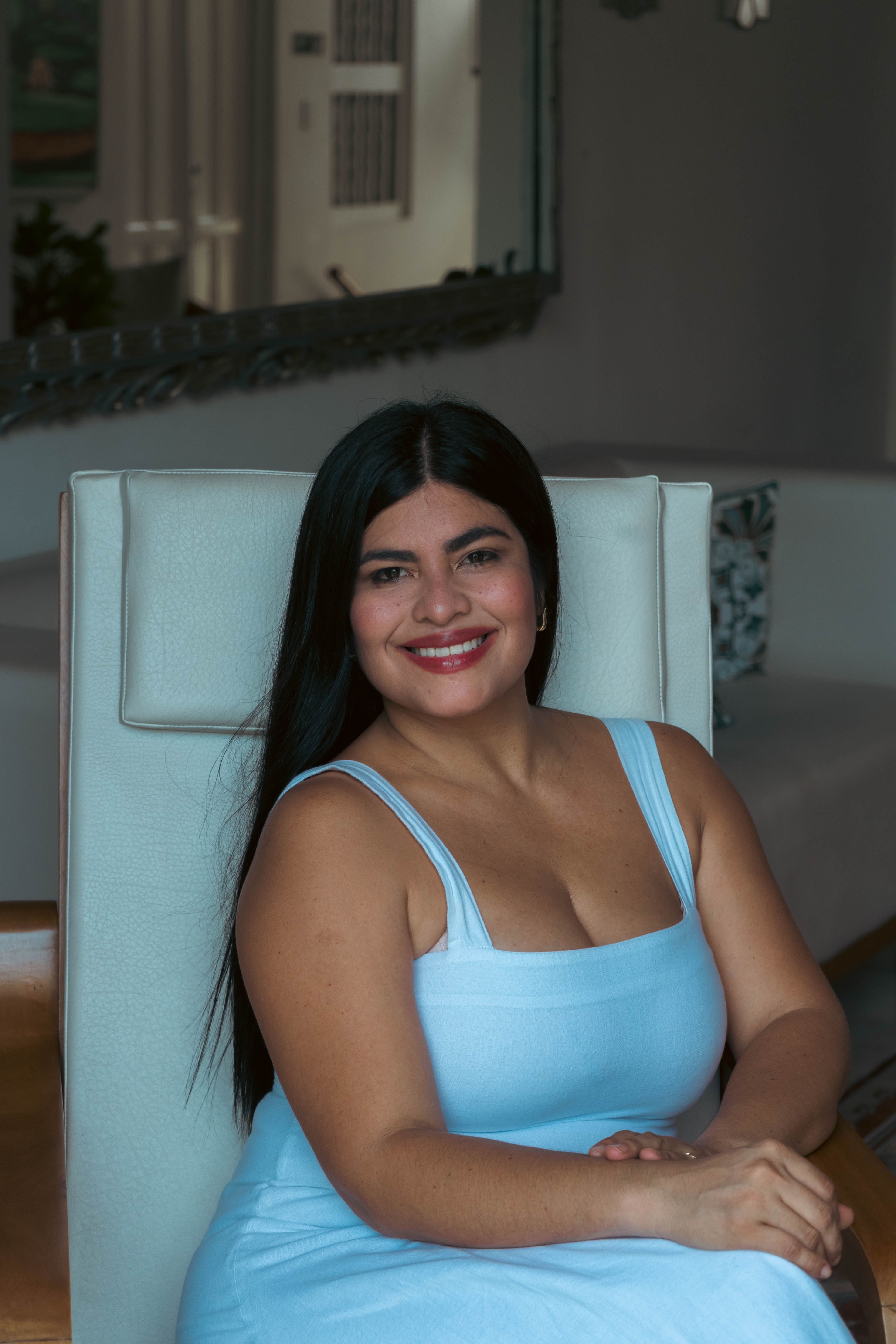 Confident woman in a blue dress smiling while sitting indoors.