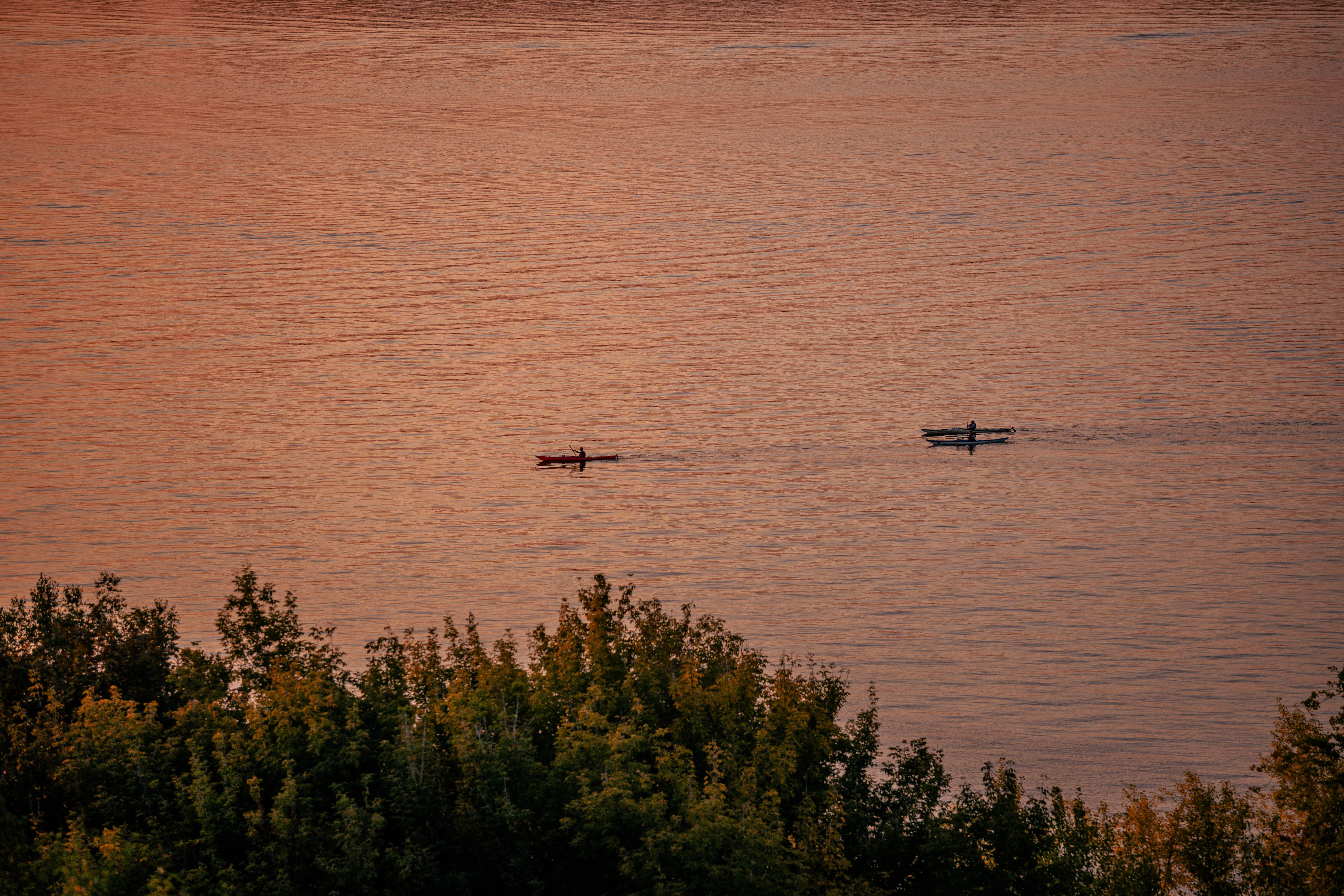 Two kayakers paddle on tranquil waters during a stunning sunset, surrounded by lush trees.