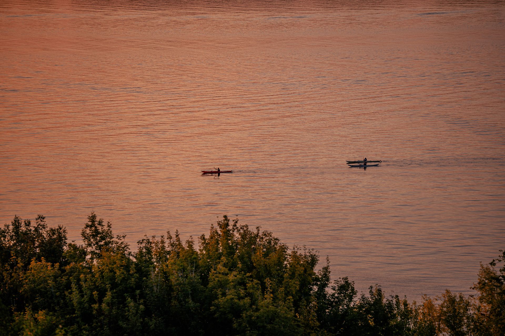 Two kayakers paddle on tranquil waters during a stunning sunset, surrounded by lush trees.