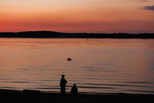 Free Silhouetted figures by a serene lake at sunset, capturing a tranquil and peaceful moment. Stock Photo