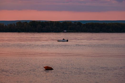 Serene sunset scene of a lone boat on a tranquil river with distant forest.