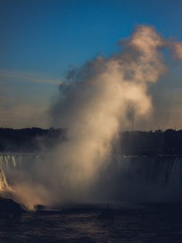 Experience the majestic Niagara Falls with a dramatic plume of mist rising into a vibrant sunset sky.