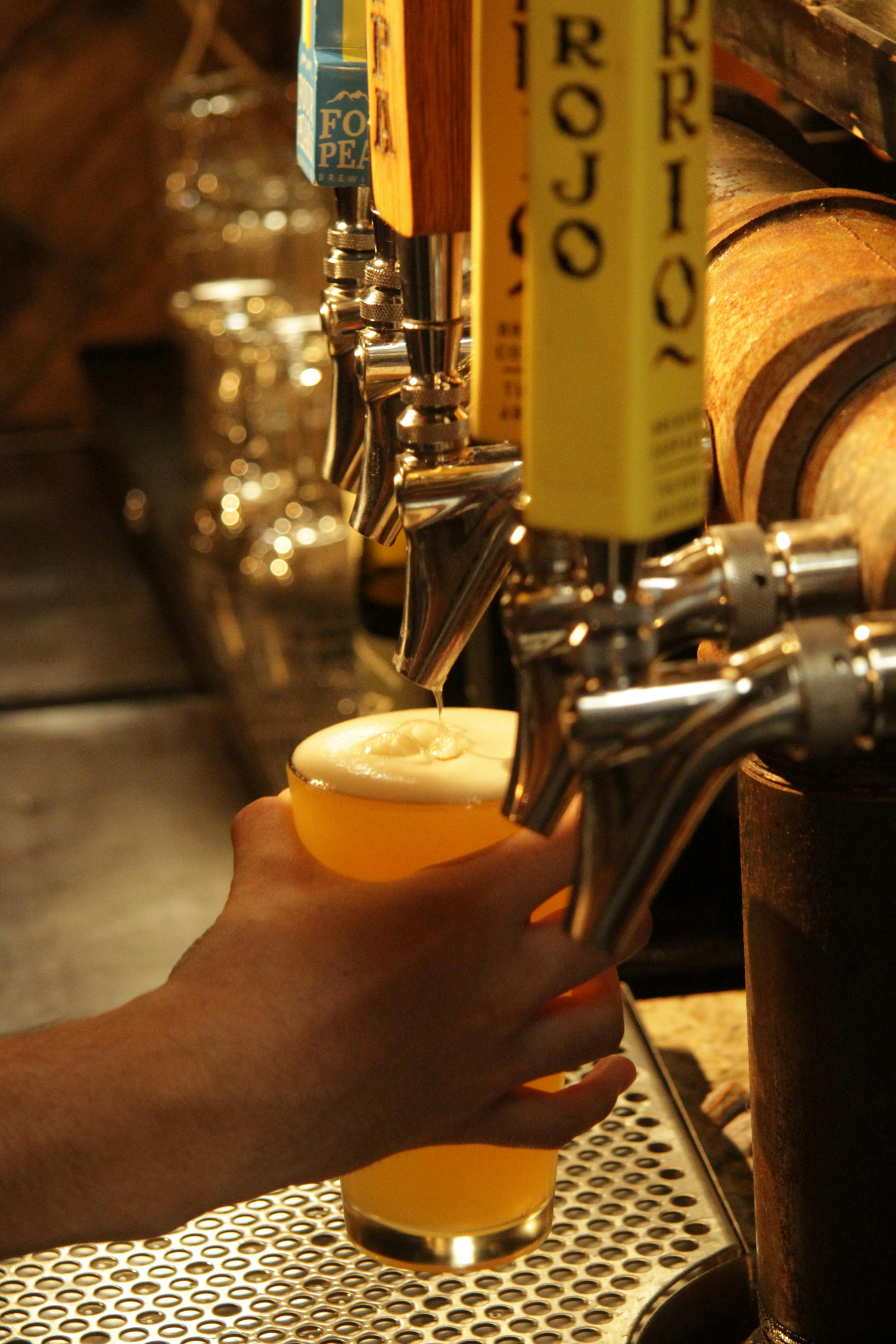 A hand pours draft beer from a tap in a Tucson, Arizona bar setting.