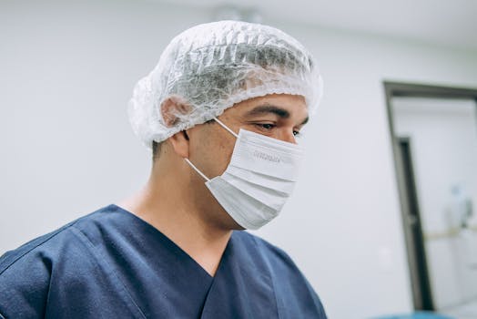 Surgeon in mask and hairnet focused in a clinical setting.