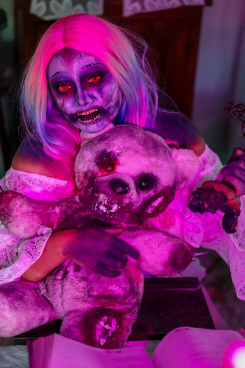 Free Zombie woman holding a spooky teddy bear under vibrant neon lighting, creating a horror-themed atmosphere. Stock Photo