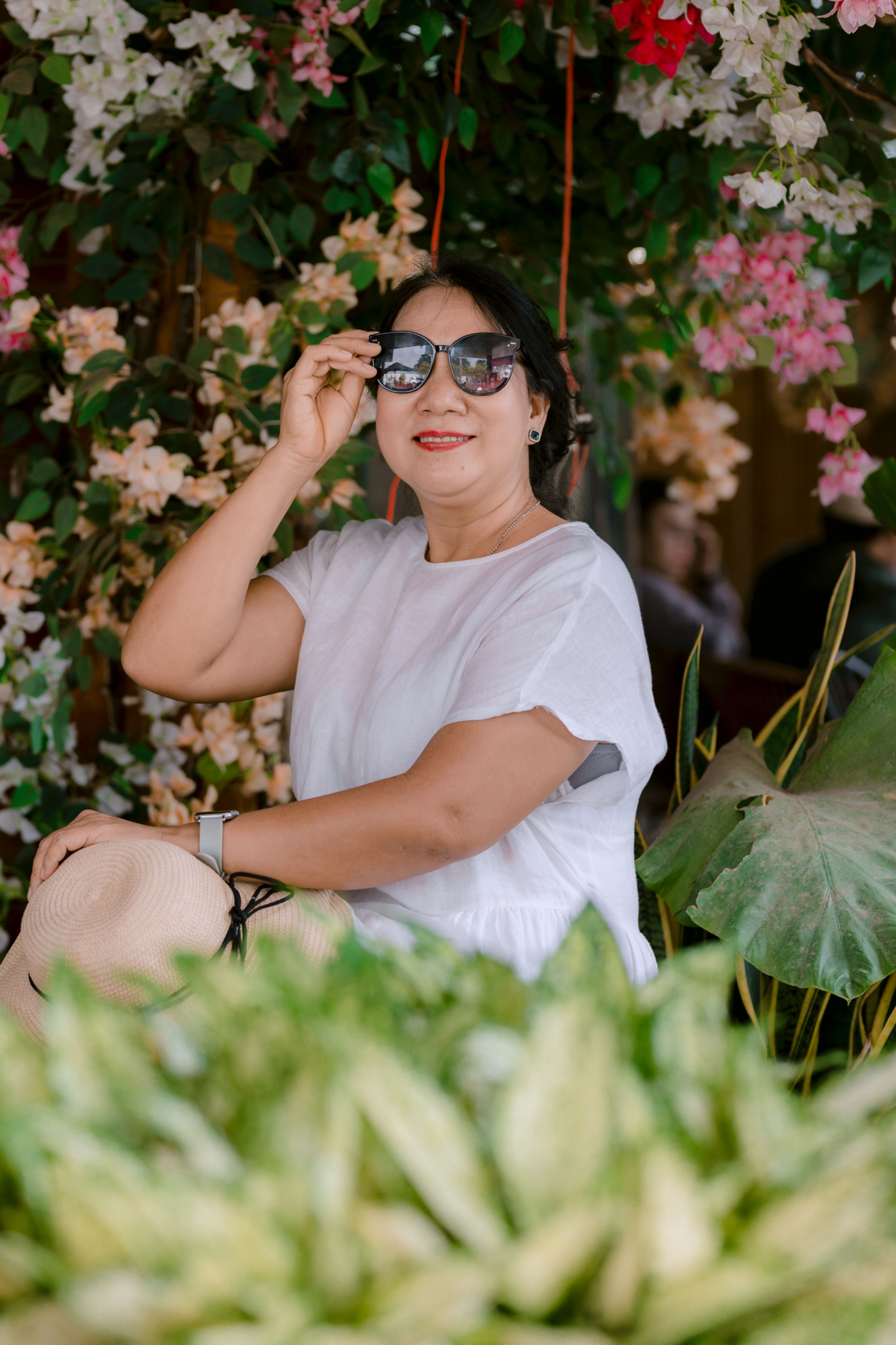 Elegant woman in sunglasses poses amid vibrant flowers, exuding style and confidence.