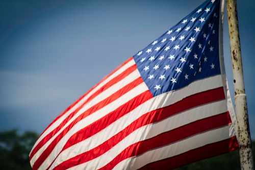 Free Vibrant American flag waving atop a flagpole against a clear blue sky. Stock Photo