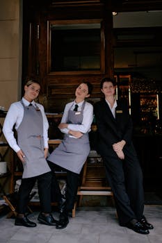 Three restaurant staff members in formal uniforms posing cheerfully in front of a restaurant.