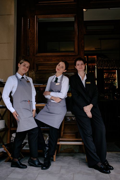 Trojica restauranskih radnika u uniformama poziraju ispred restorana