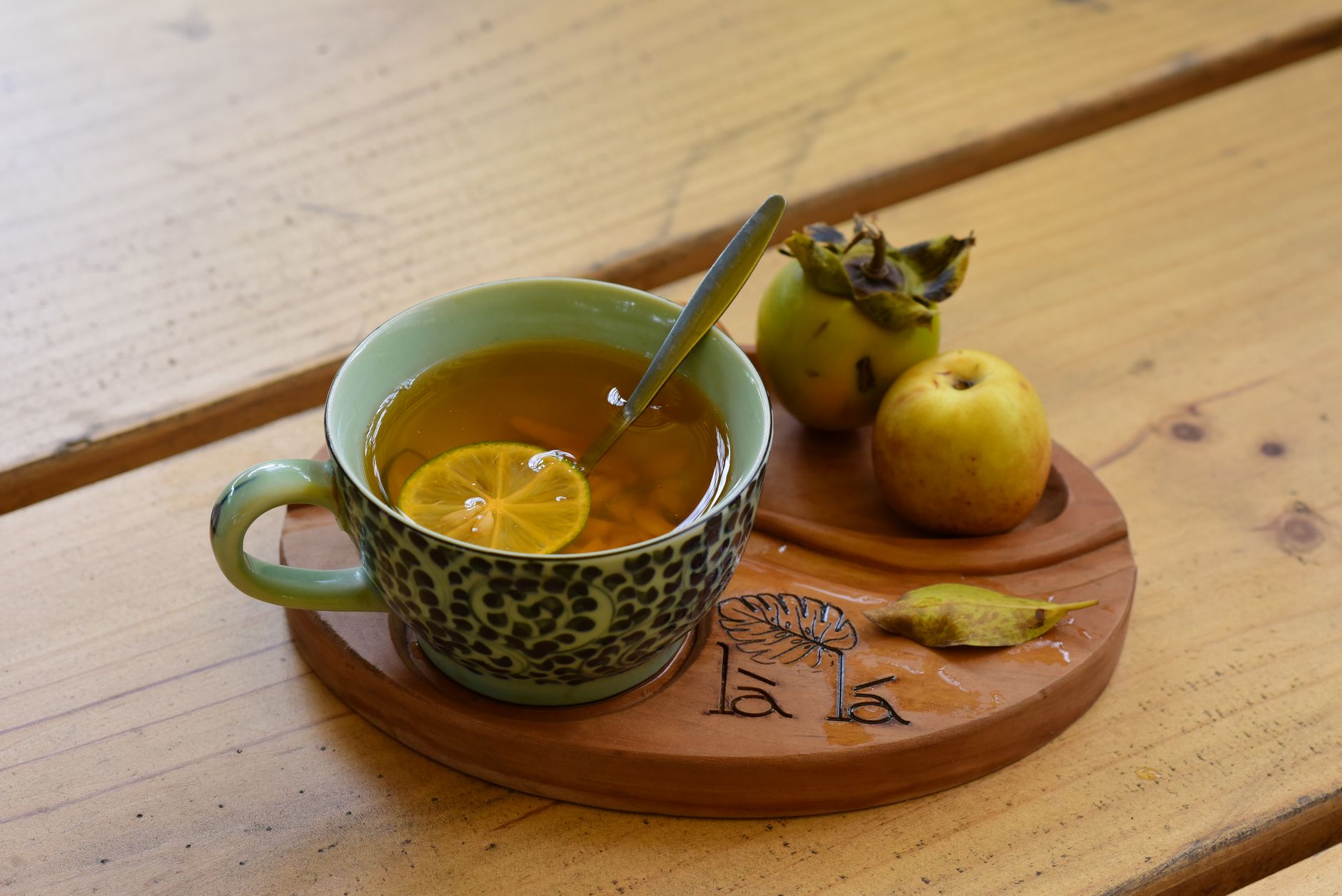 trà kombucha dưỡng nhan - Một tách trà thảo mộc ấm với chanh, được phục vụ kèm táo và hồng trên khay gỗ.