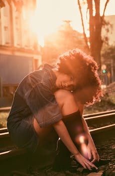 A beautiful woman with curly hair sitting on railroad tracks in warm sunset light.