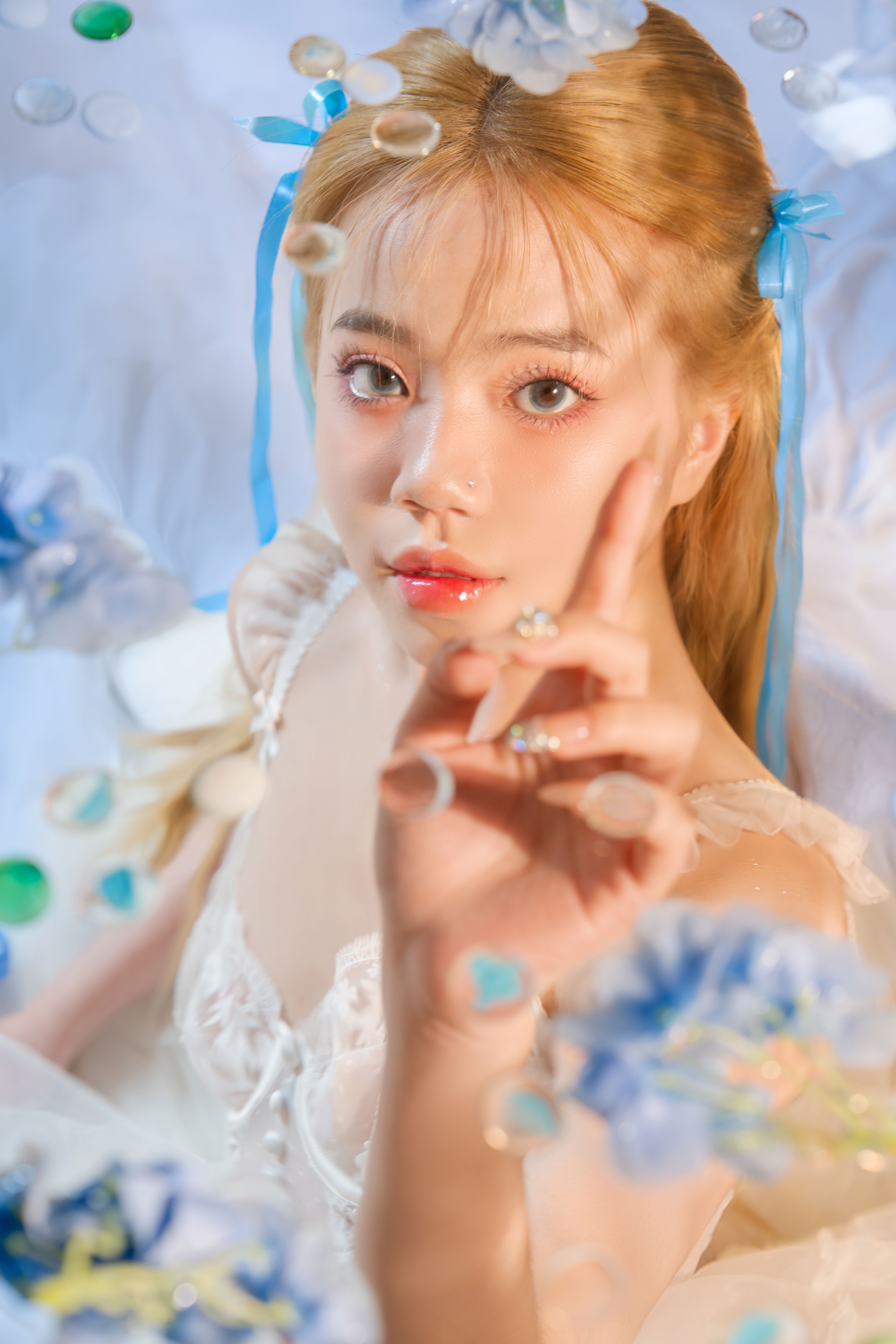 Artistic portrait of a young woman surrounded by blue flowers and soft lighting.