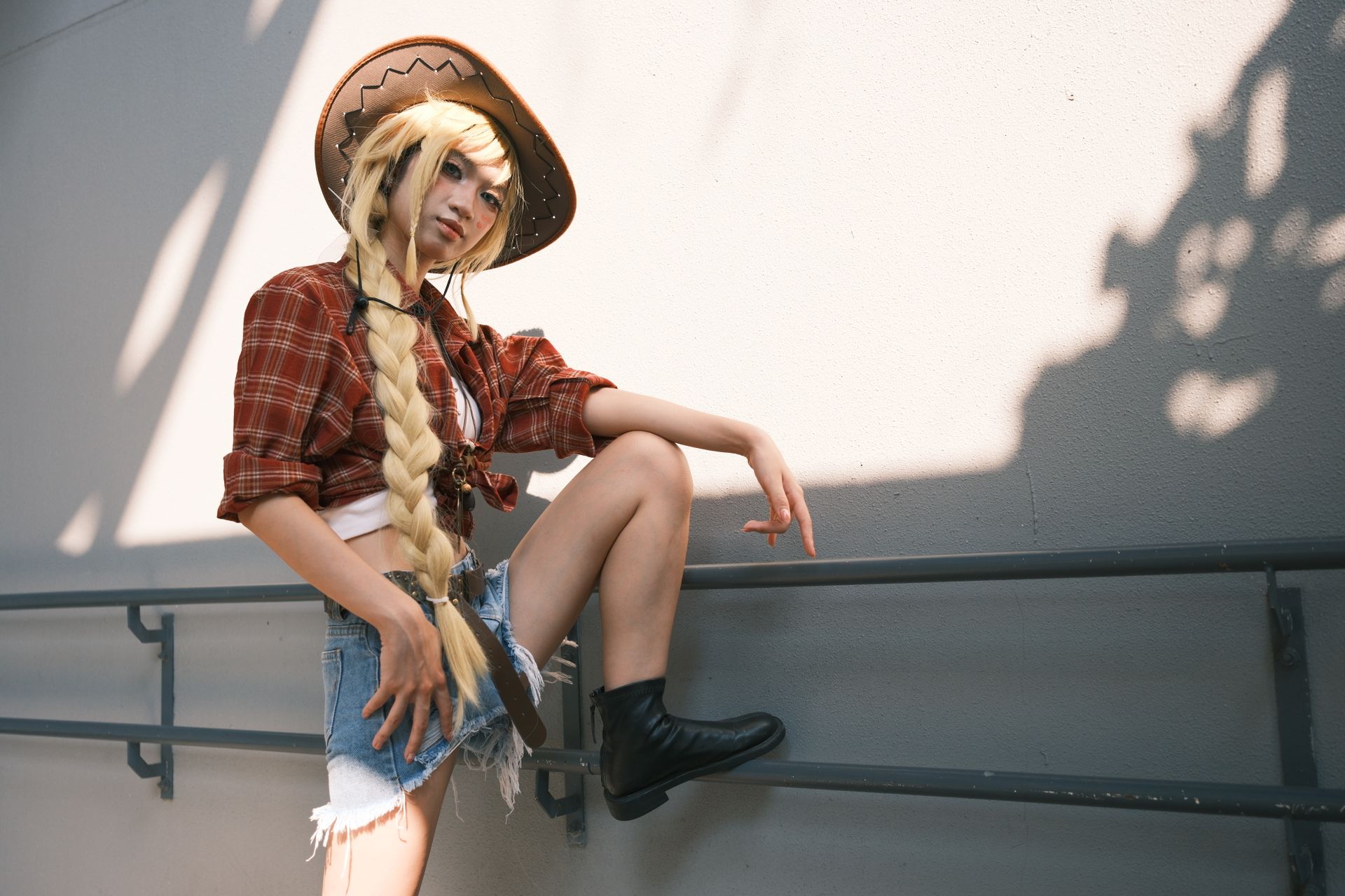 A young woman in a cowboy hat and plaid shirt poses outdoors, embodying a playful Western style.